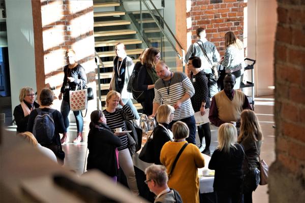 Publik på seminariet i solig foajé. Seminaariyleisö aurinkoisessa aulassa.