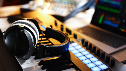 Hörlurar på ett MIDI-keyboard i en musikstudio, med ljudutrustning i bakgrunden. Kuulokkeet MIDI-koskettimiston päällä musiikkistudiossa, taustalla äänilaitteita.