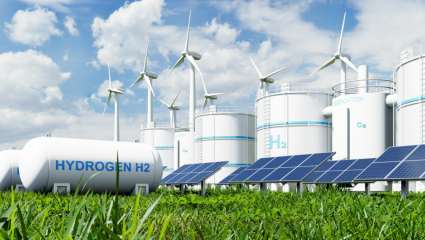 Vätgas- och energianläggning med stora H2-tankar, vindkraftverk och solpaneler i ett grönt landskap. Vety- ja energiantuotantolaitos, jossa on suuria H2-säiliöitä, tuulivoimaloita ja aurinkopaneeleja vihreässä maisemassa.