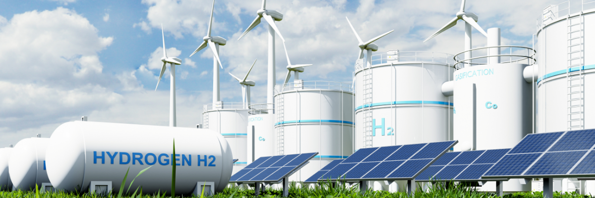 Vätgas- och energianläggning med stora H2-tankar, vindkraftverk och solpaneler i ett grönt landskap. Vety- ja energiantuotantolaitos, jossa on suuria H2-säiliöitä, tuulivoimaloita ja aurinkopaneeleja vihreässä maisemassa.