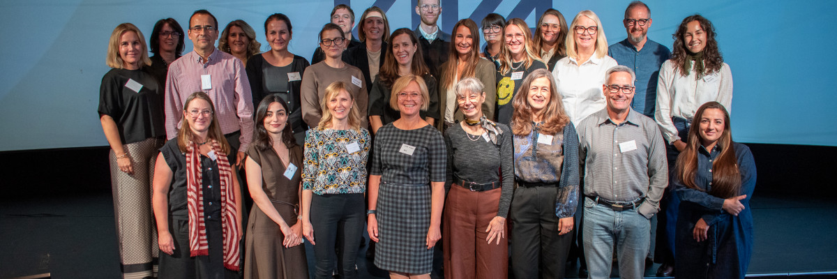 Group photo of conference participants standing on a stage in front of a blue presentation screen.