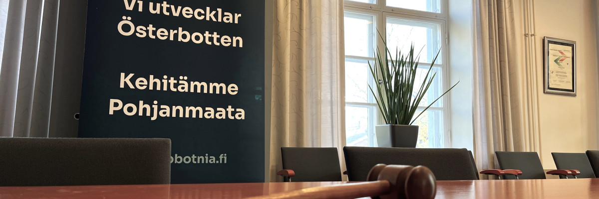 Klubba på mötesbord i Österbottens förbunds sammanträdesrum. I bakgrunden syns en rollup med texten ”Vi utvecklar Österbotten”. Nuija Pohjanmaan liiton kokoushuoneen pöydällä. Taustalla näkyy roll-up, jossa lukee ”Kehitämme Pohjanmaata”.