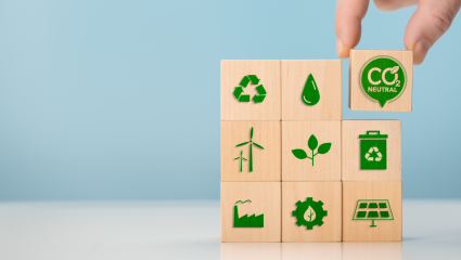 Hand staplar träklossar med miljösymboler som återvinning, förnybar energi och CO₂-neutral. Käsi pinoaa puupalikoita, joissa on ympäristösymboleja kuten kierrätys, uusiutuva energia ja CO₂-neutraalius.
