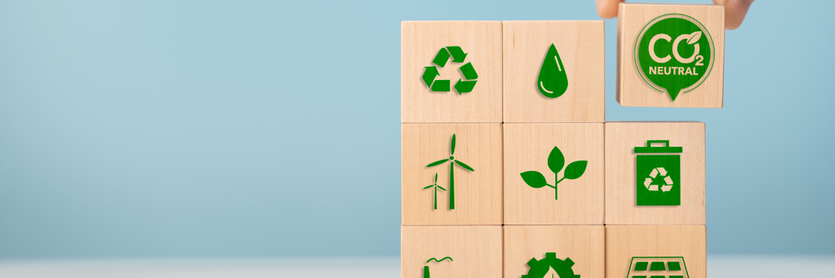 Hand staplar träklossar med miljösymboler som återvinning, förnybar energi och CO₂-neutral. Käsi pinoaa puupalikoita, joissa on ympäristösymboleja kuten kierrätys, uusiutuva energia ja CO₂-neutraalius.